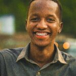 Close-up of a smiling man with braces enjoying a sunny day outdoors.