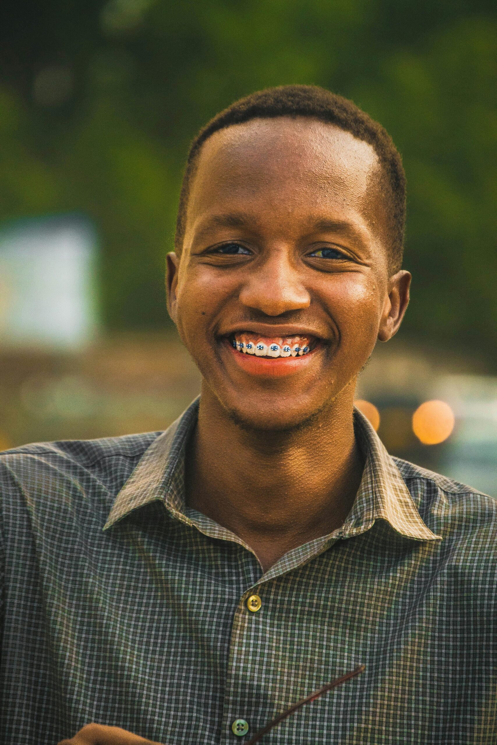 Close-up of a smiling man with braces enjoying a sunny day outdoors.