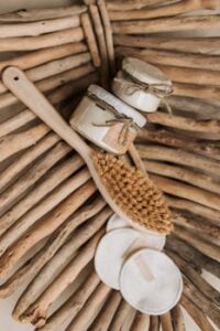Natural skincare products with a wooden brush and reusable pads on driftwood.